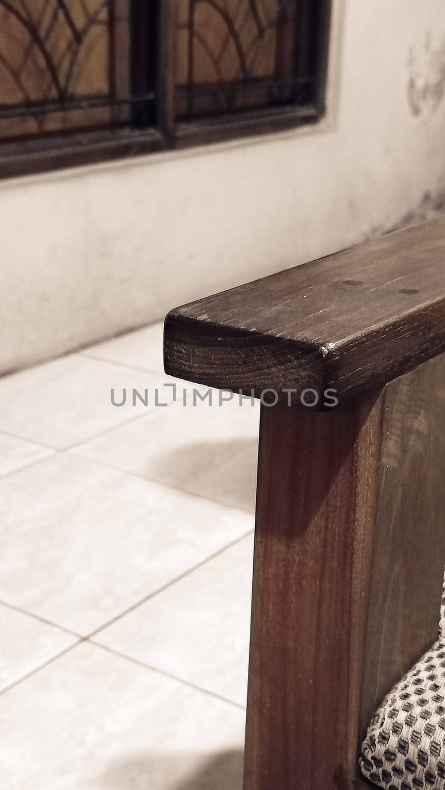 A detailed view of a wooden chair armrest, highlighting its texture and design. The cozy indoor setting includes tiled flooring and a window.