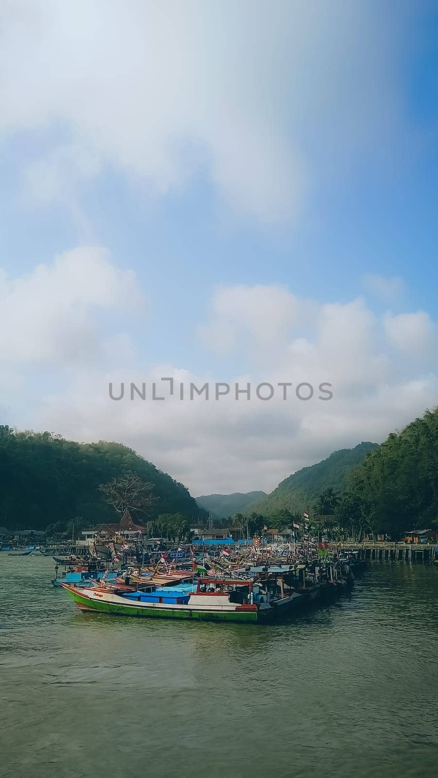 A large group of boats are floating on a lake. The sky is blue with some clouds