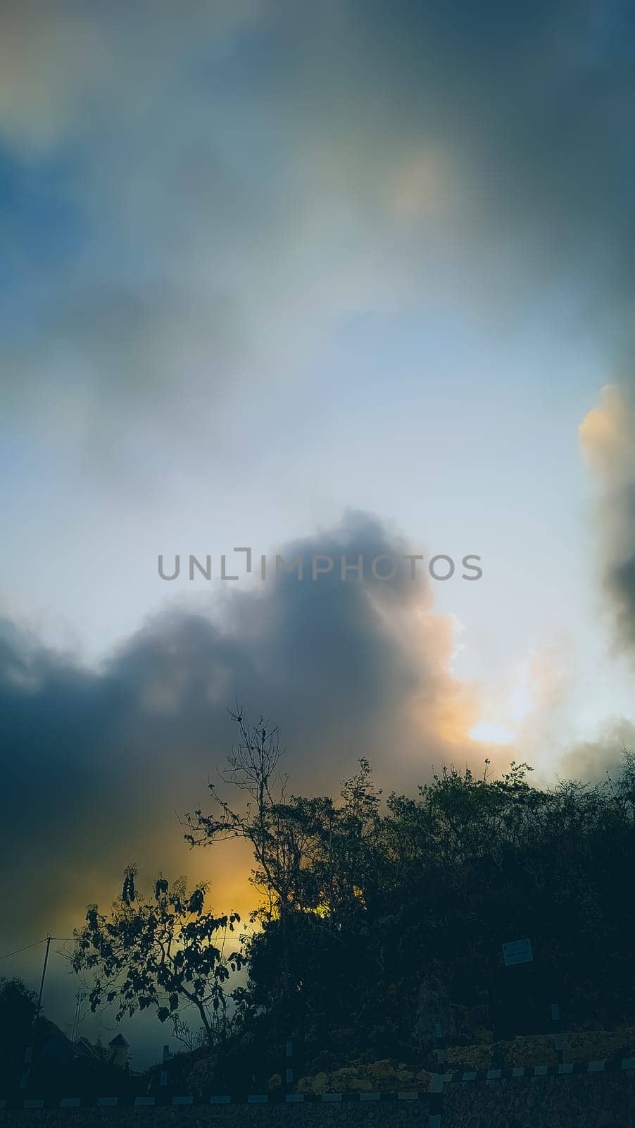 Captivating sunset scene with a silhouette of trees against dramatic, colorful clouds. The warm tones evoke feelings of tranquility and peace, offering a perfect example of nature's breathtaking beauty.