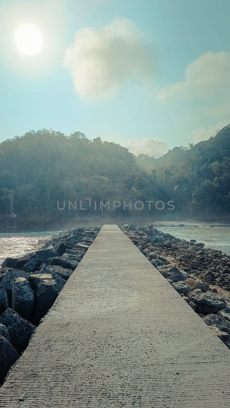 A rocky shoreline with a large rock formation in the background. The water is calm and the sky is blue