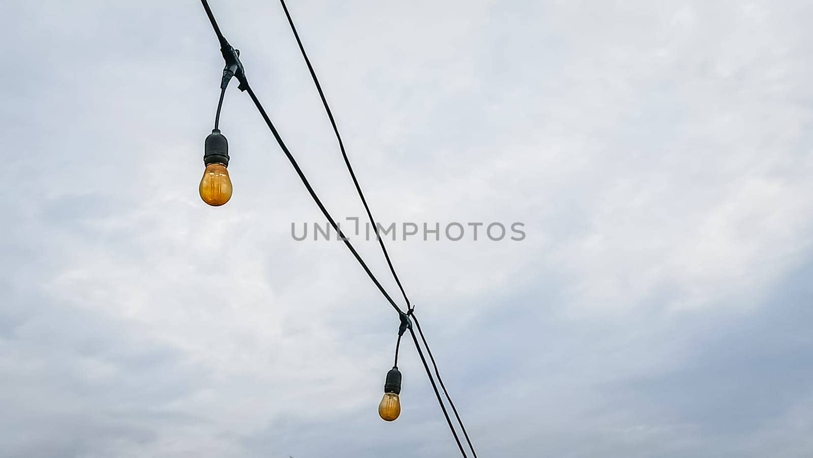 A string of lights hanging from a power line. The lights are yellow and are hanging from the wires