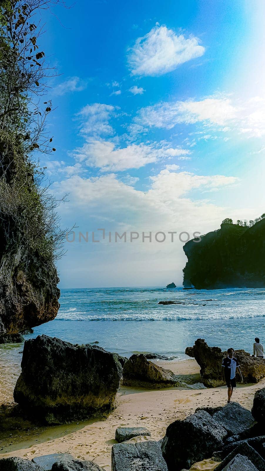 A rocky shoreline with a large rock formation in the background. The water is calm and the sky is blue