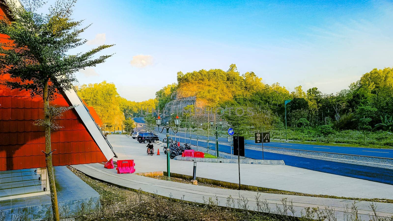 A peaceful roadside view featuring a red-roofed building, clear blue sky, and greenery along a mountain road, creating a tranquil atmosphere.