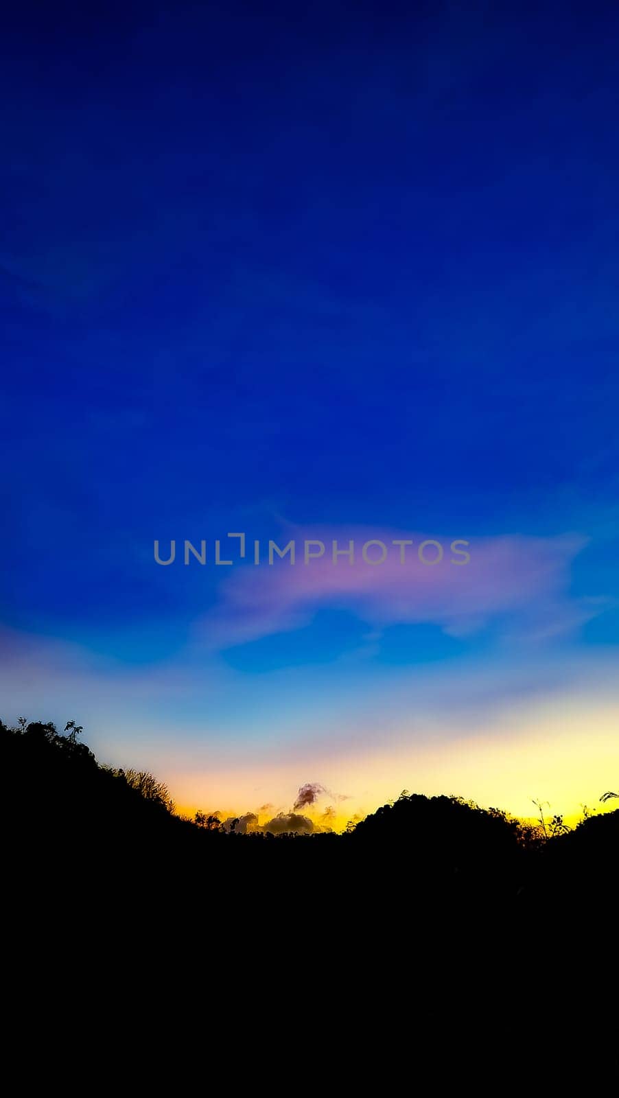 A picturesque silhouette of a landscape set against a vibrant sunset sky, showcasing a blend of blue, orange, and yellow hues. Perfect for themes of nature, tranquility, and beauty.