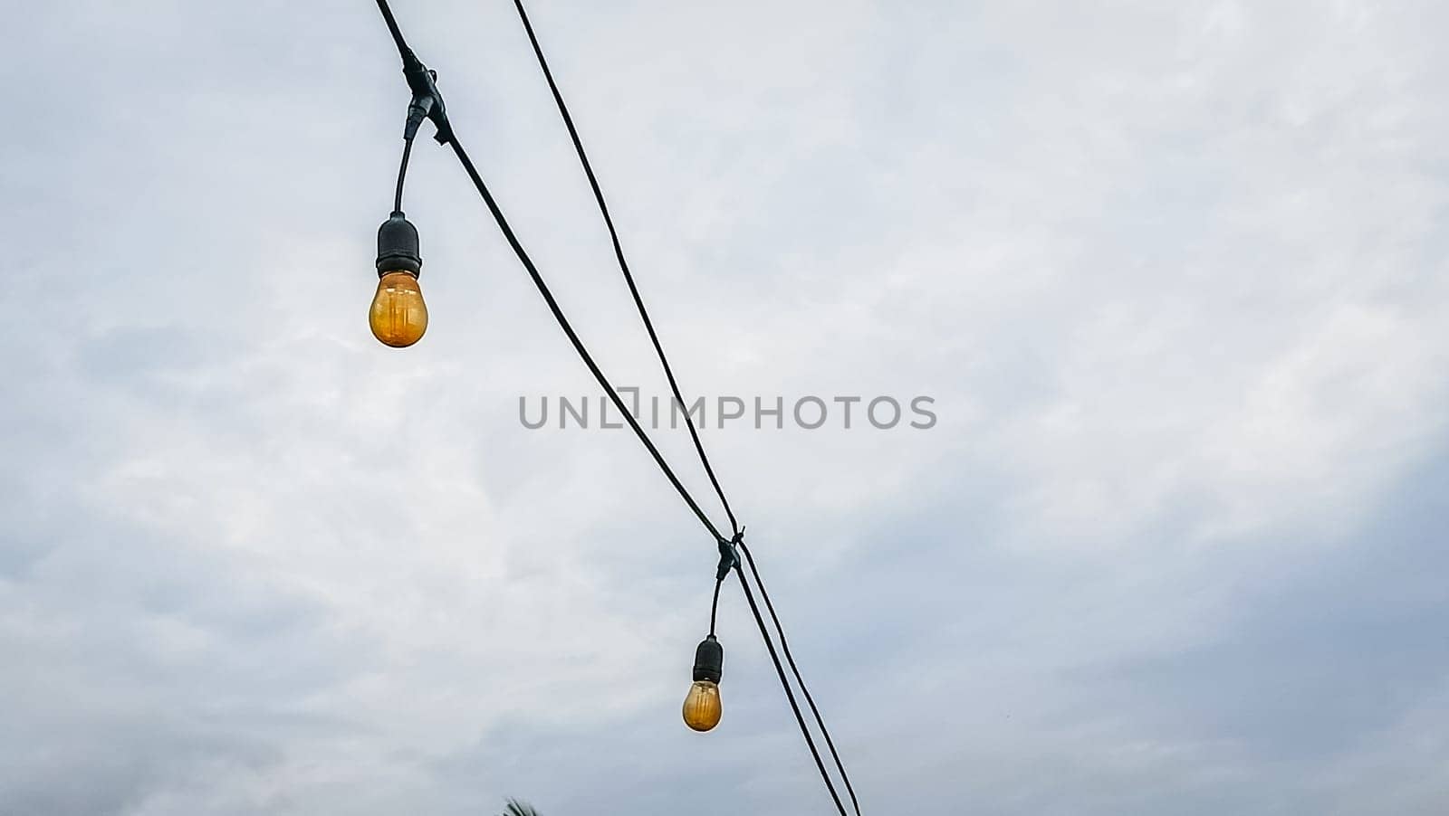A string of lights hanging from a power line. The lights are yellow and are hanging from the wires