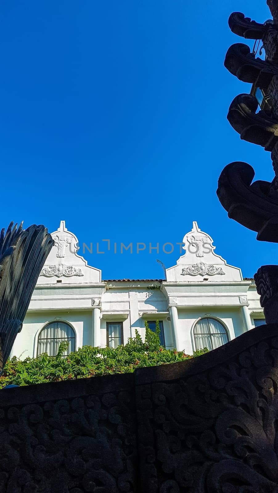 A stunning colonial building with intricate architectural details. Vibrant greenery adds charm against a clear blue sky. Perfect for concepts of history, architecture, and nature in harmony.