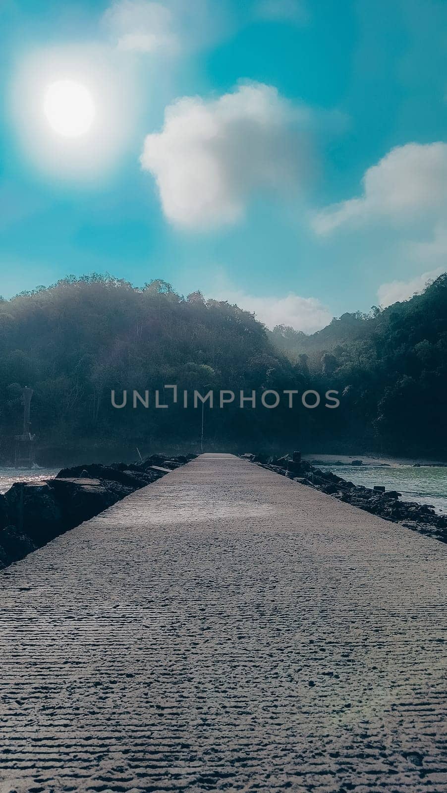 A rocky shoreline with a large rock formation in the background. The water is calm and the sky is blue