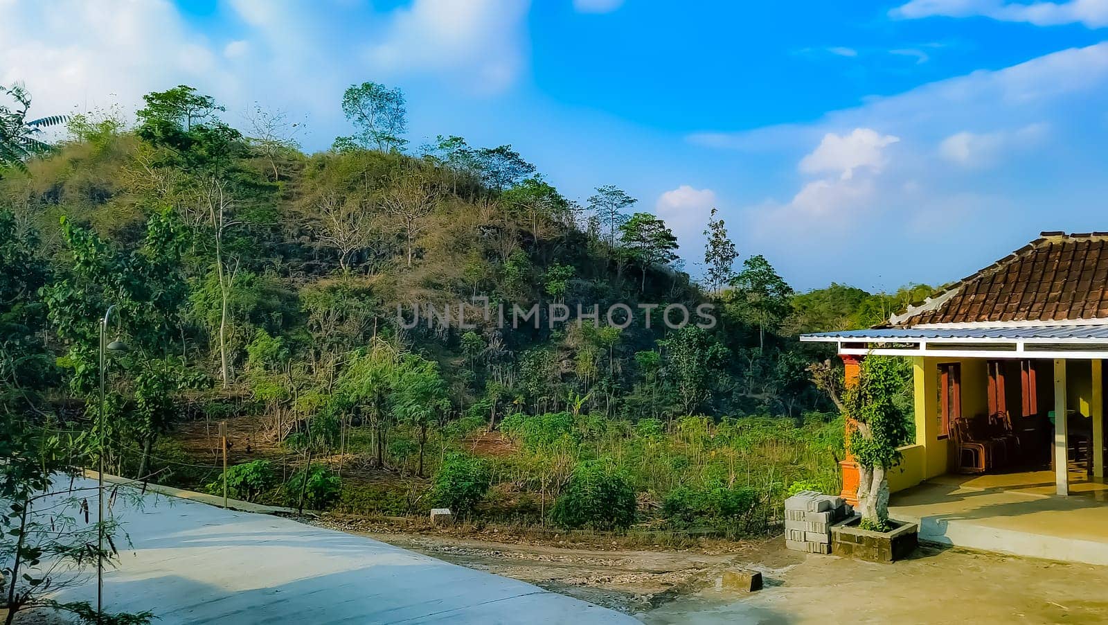 A serene countryside house surrounded by lush vegetation and rolling hills under a bright blue sky, evoking tranquility and natural beauty.