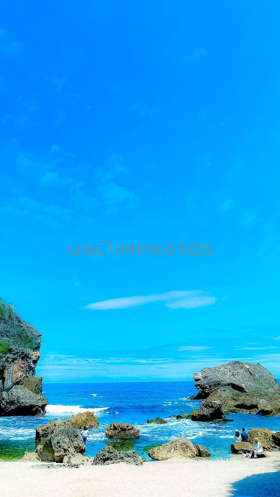 A serene beach setting with clear blue skies, rocks, and gentle sea waves. Perfect for representing relaxation, nature, and tranquility in a coastal environment.