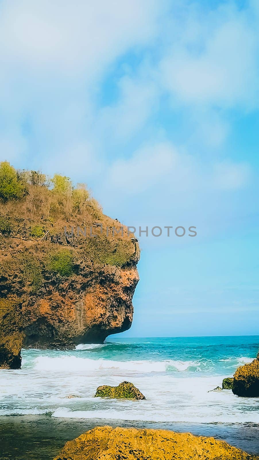 A serene beach setting with clear blue skies, rocks, and gentle sea waves. Perfect for representing relaxation, nature, and tranquility in a coastal environment.