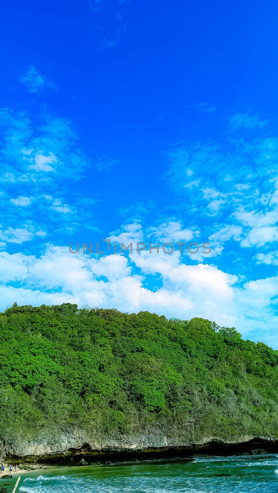 A rocky shoreline with a large rock formation in the background. The water is calm and the sky is blue