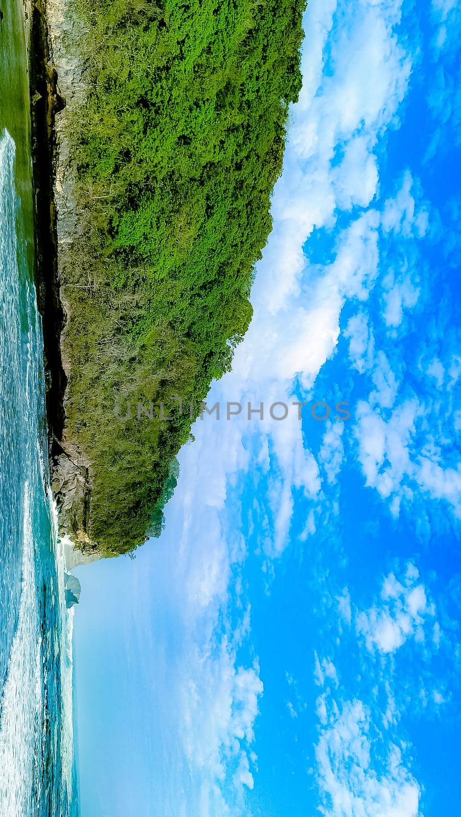 A rocky shoreline with a large rock formation in the background. The water is calm and the sky is blue