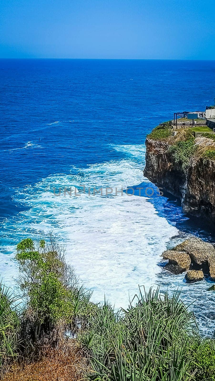 Stunning view of a rocky cliff overlooking the vast, blue ocean with waves crashing below. The harmonious blend of sea and sky offers a sense of peace and tranquility.