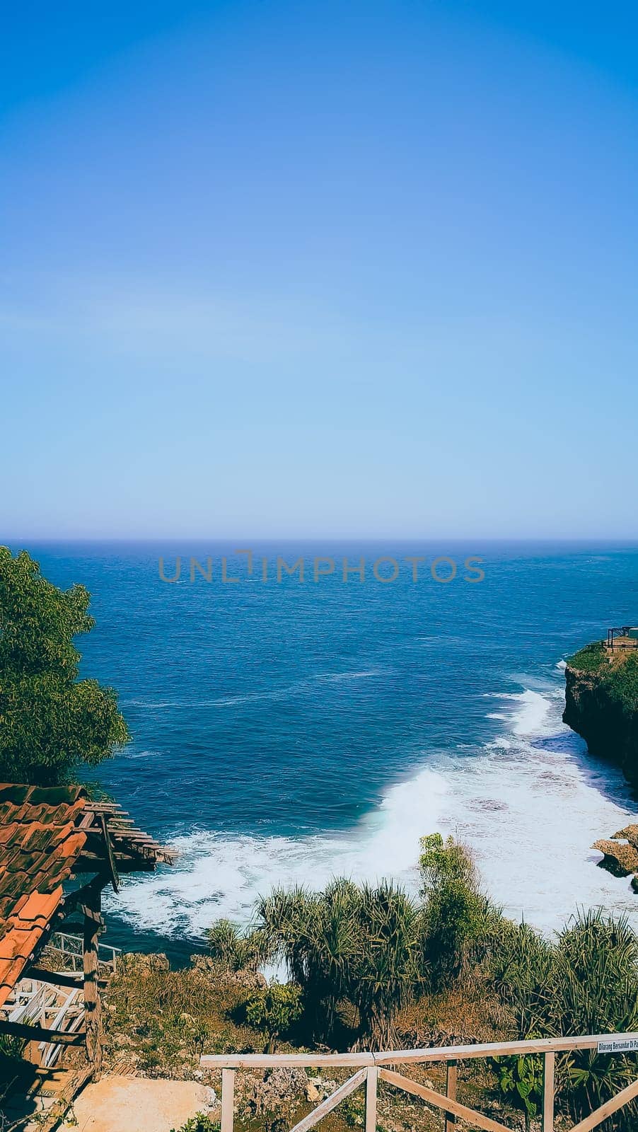 Stunning view of a rocky cliff overlooking the vast, blue ocean with waves crashing below. The harmonious blend of sea and sky offers a sense of peace and tranquility.