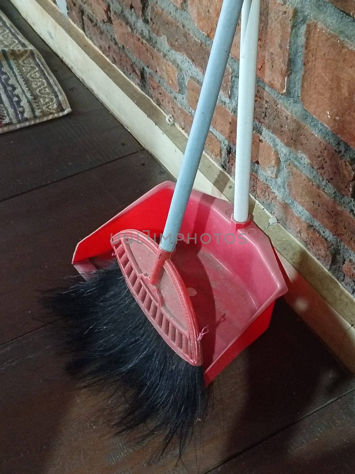 A red dustpan and broom resting against a rustic brick wall, creating a cozy and practical cleaning setup. Perfect for housekeeping and cleaning concepts.