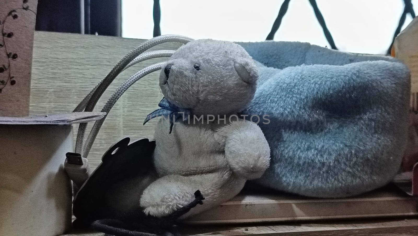 A teddy bear is sitting on a wooden surface next to a blue blanket. The scene is cozy and inviting, with the teddy bear looking up at the camera