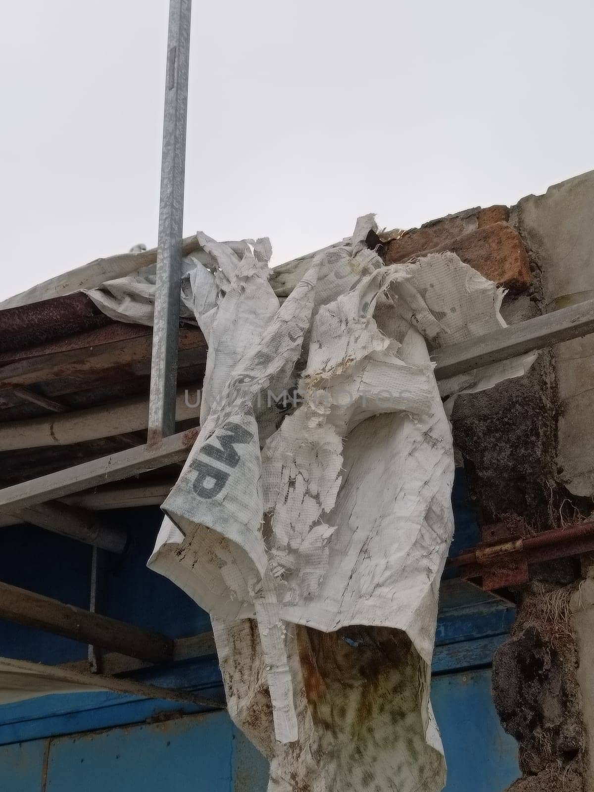 A tattered tarpaulin hangs on a rustic building, conveying deterioration and abandonment. Its worn texture tells a story of weather exposure and decay at a desolate construction site.