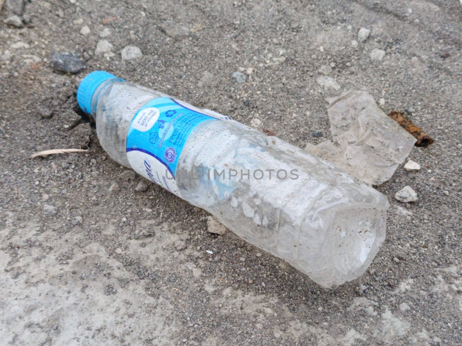 A crumpled plastic bottle lies on gravel, highlighting environmental pollution. This image represents littering, waste, and the need for ecological awareness and recycling efforts.