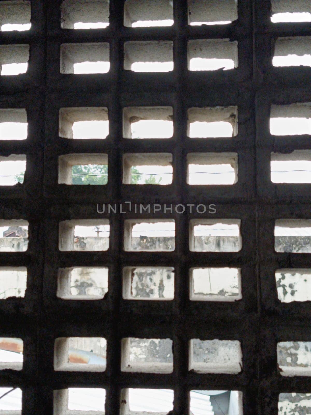 Abstract view through a grid of concrete blocks, showcasing the interplay of light and shadow. The geometric pattern offers an industrial and textured aesthetic, creating a sense of confinement and openness.