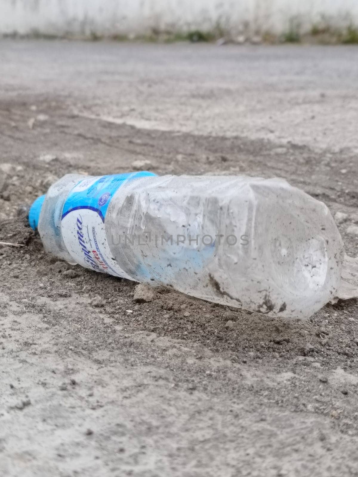 A crumpled plastic bottle lies on gravel, highlighting environmental pollution. This image represents littering, waste, and the need for ecological awareness and recycling efforts.