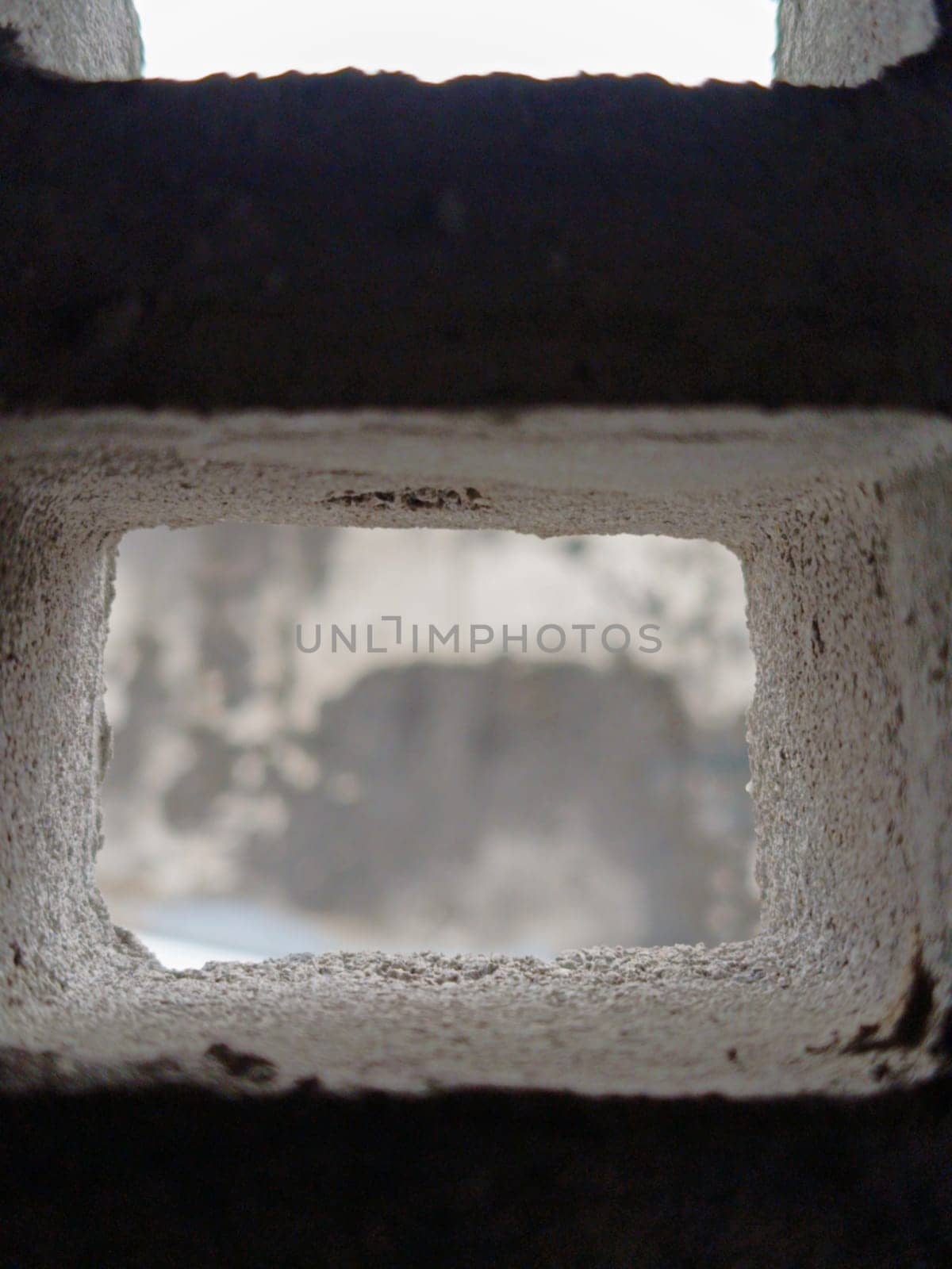 Abstract view through a grid of concrete blocks, showcasing the interplay of light and shadow. The geometric pattern offers an industrial and textured aesthetic, creating a sense of confinement and openness.