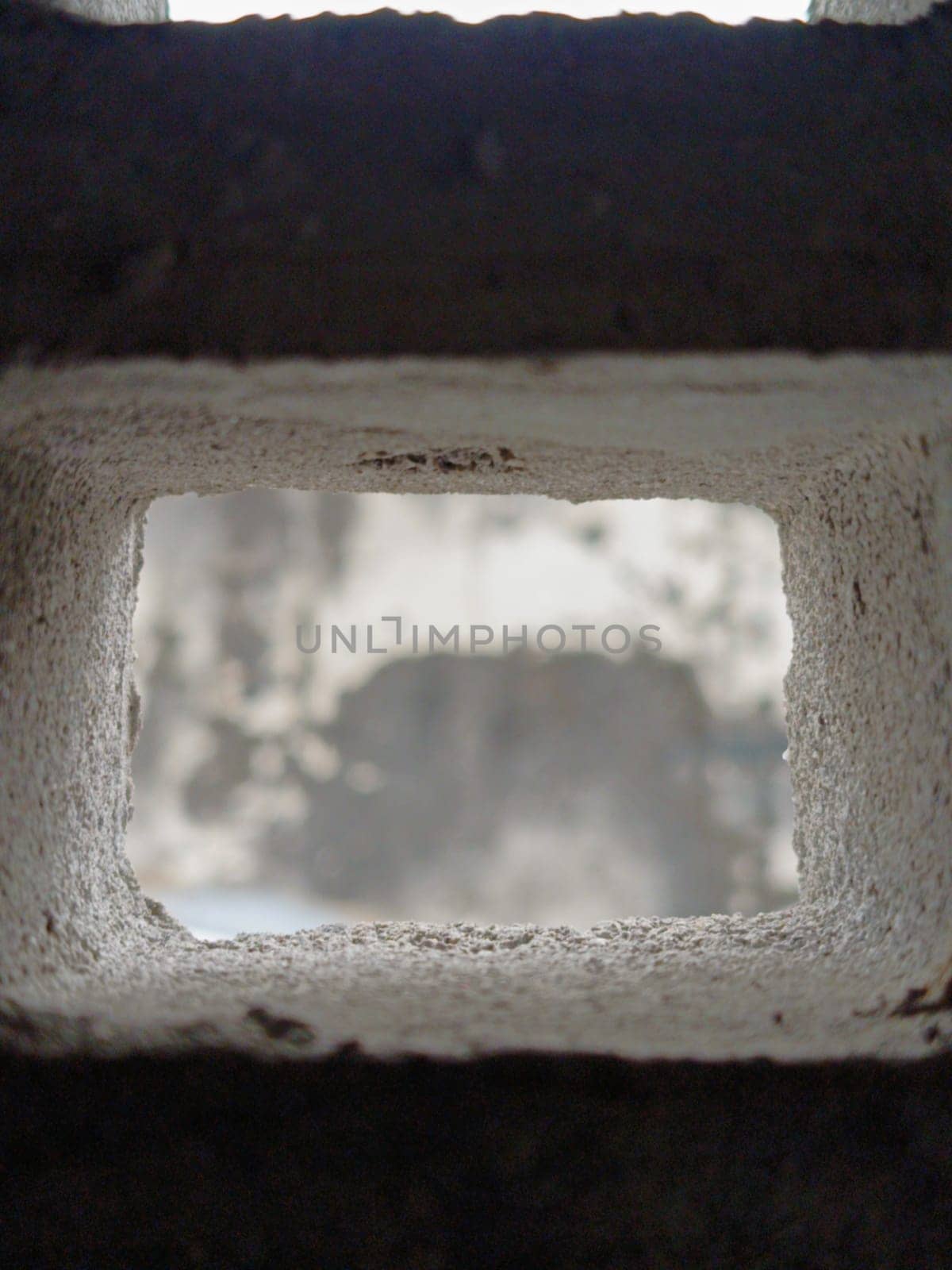 Abstract view through a grid of concrete blocks, showcasing the interplay of light and shadow. The geometric pattern offers an industrial and textured aesthetic, creating a sense of confinement and openness.