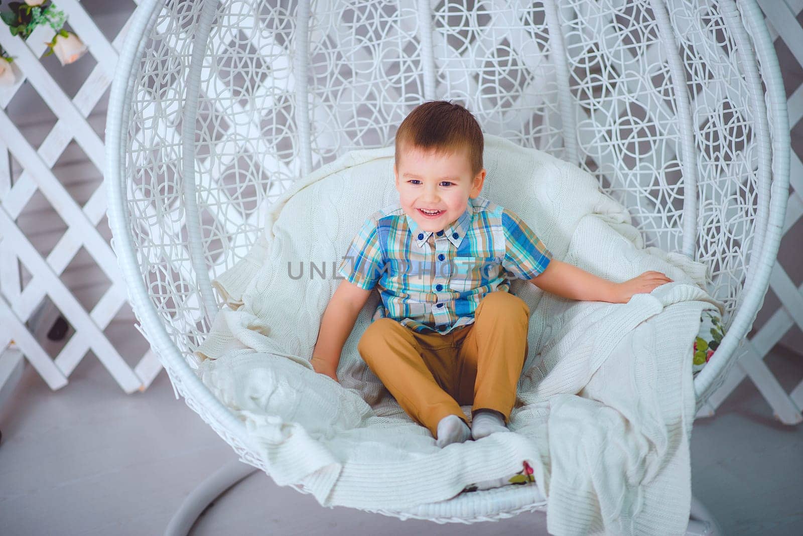 A cheerful young boy with a bright smile is happily sitting in a stylish and cozy hanging egg chair