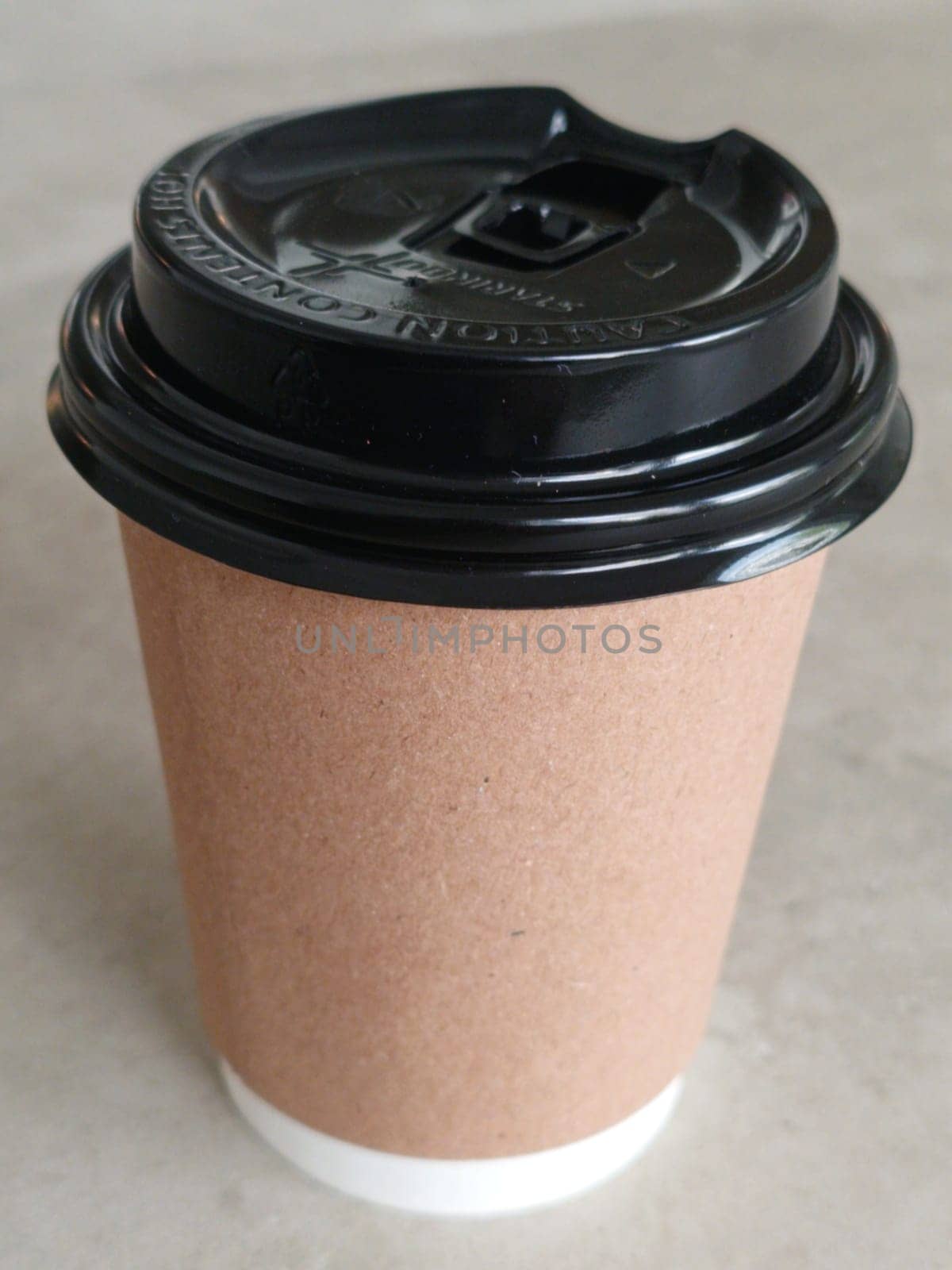 Simple brown paper coffee cup with black plastic lid, ideal for takeaway beverages. Represents convenience, modern lifestyle, and daily routines. Perfect for cafes and coffee shops imagery.