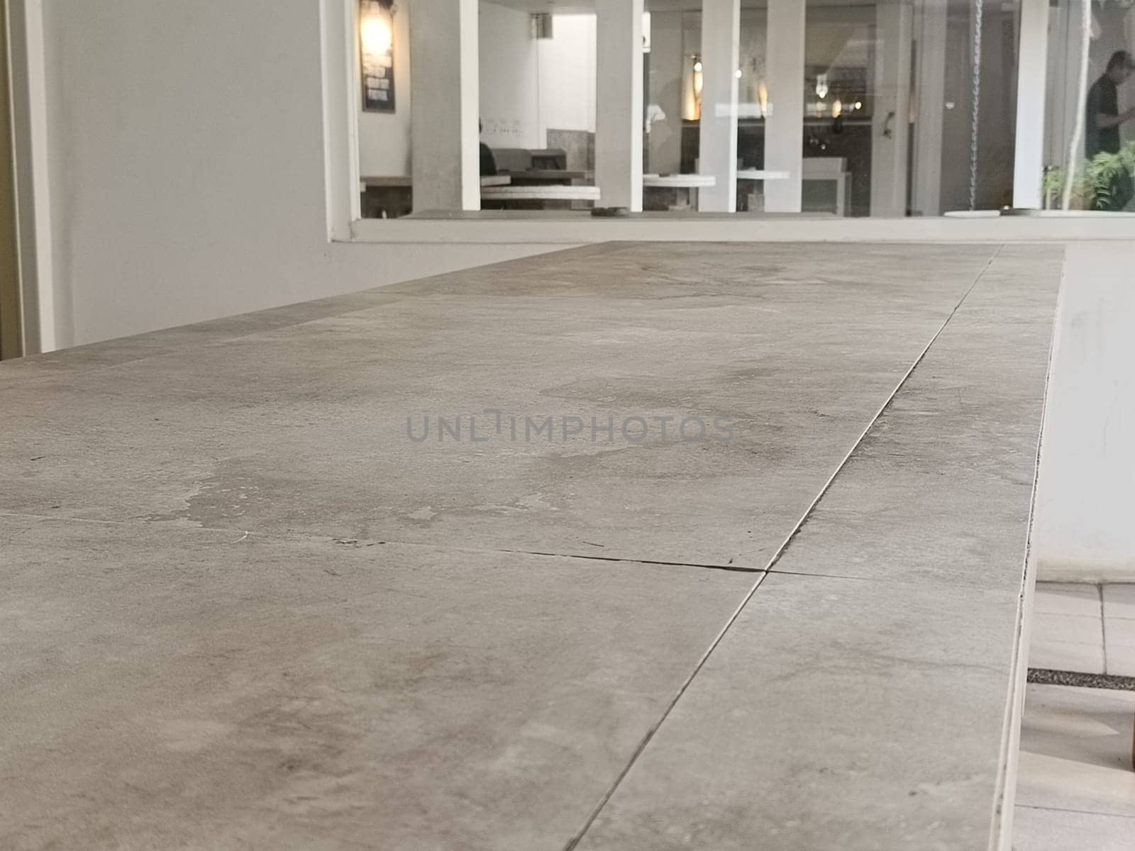 A modern minimalist cafe interior featuring a large concrete table and greenery. The bright space is filled with natural light, providing a serene and inviting atmosphere.