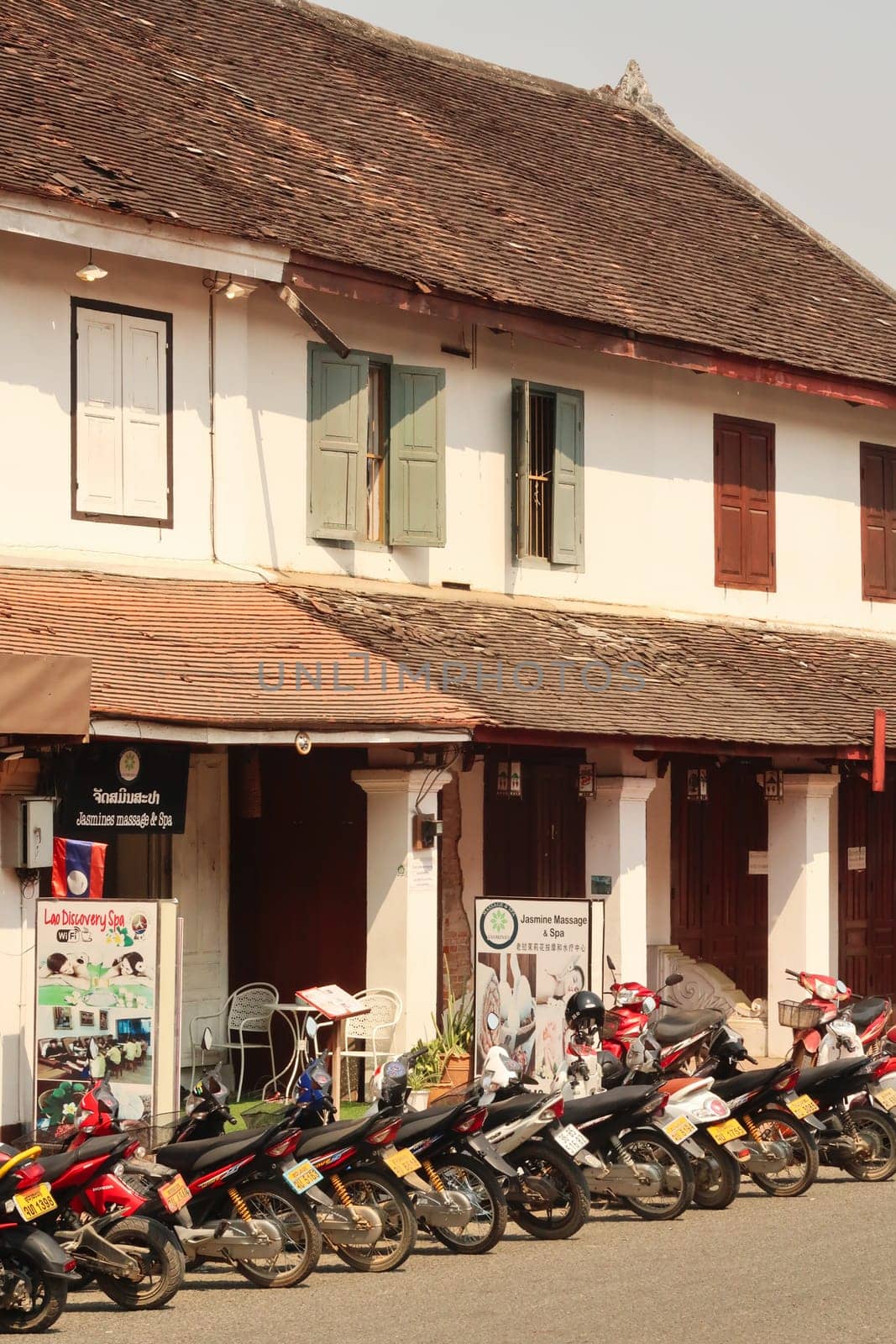 Many motorbikes are parked in front of a traditional, colonial house in the old town of Luang Prabang, Laos 2023