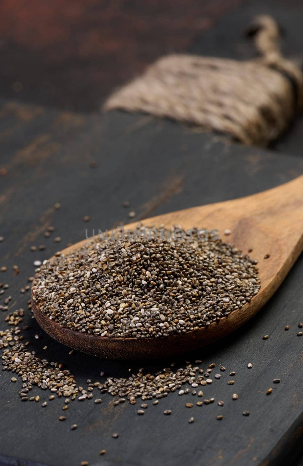 Chia seeds in a wooden spoon on a black table, close up