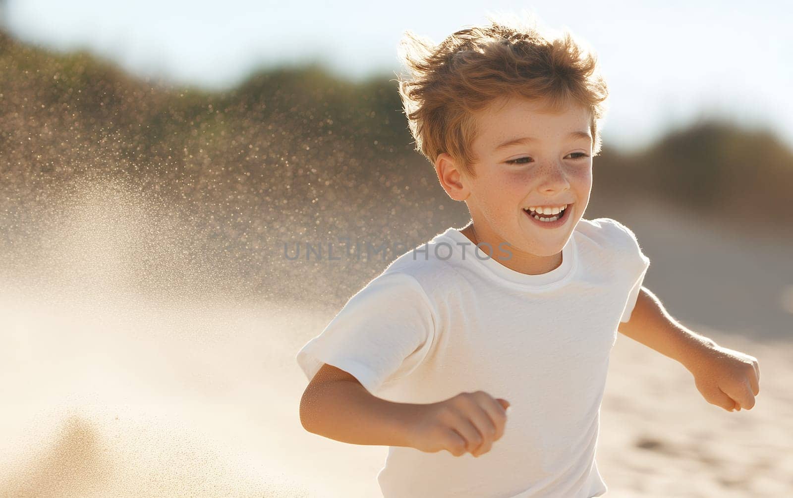 Joyful young boy running on a sandy beach, kicking up sand as he enjoys a sunny day.