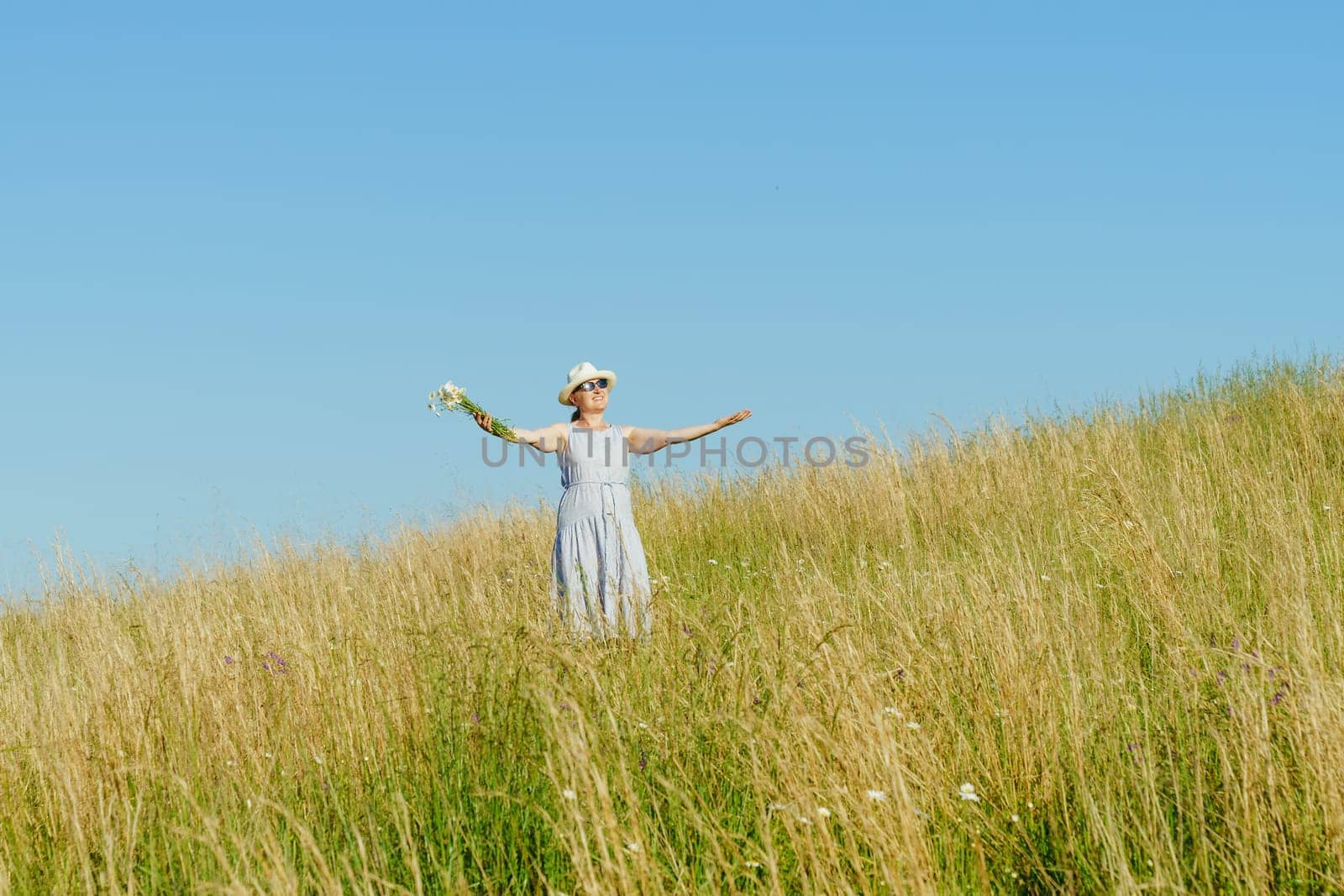 Happy mature woman with wildflowers in a tall grass field on a bright summer day.