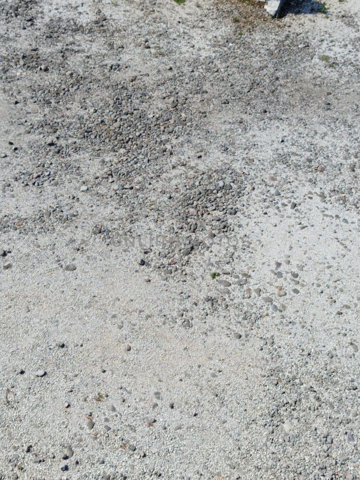 Close-up view of a gravel surface featuring scattered rocks and pebbles displaying an earthy texture under sunlight. Ideal for backgrounds and design projects.