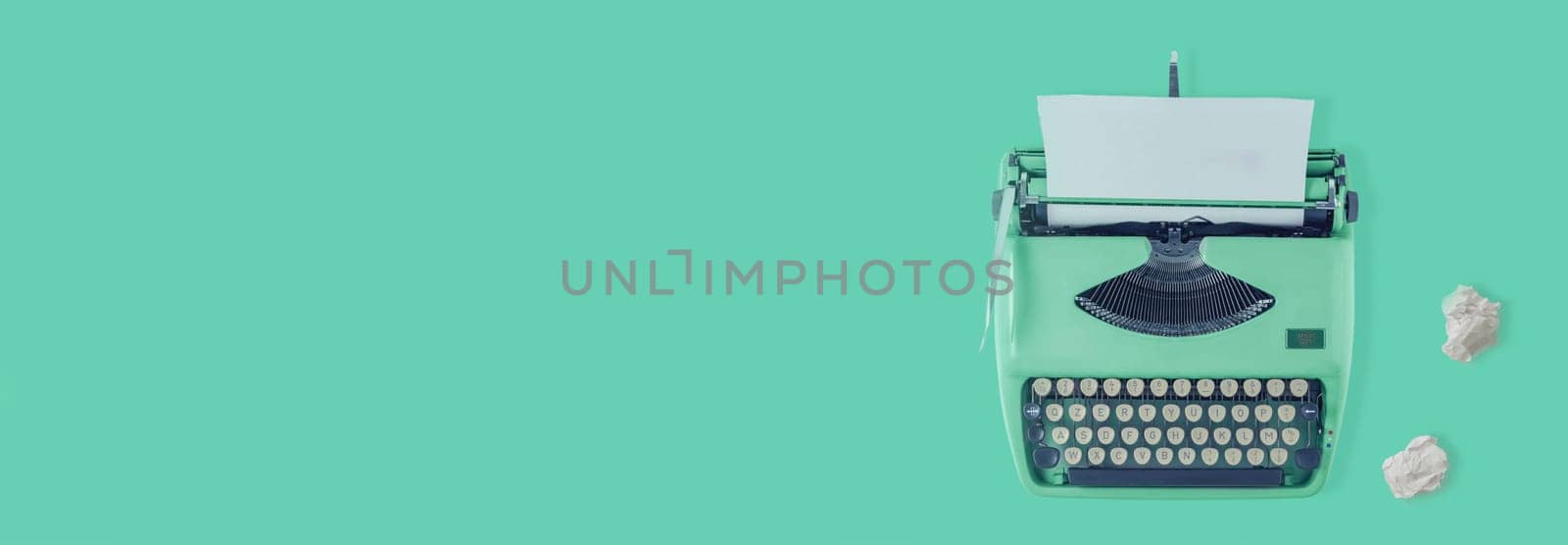 A green vintage typewriter with green background and two paper balls.
