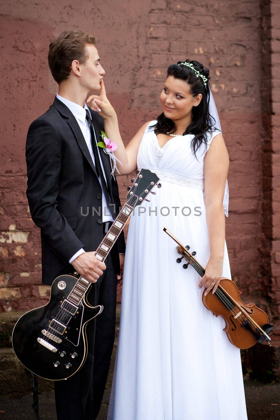 A joyful couple in elegant wedding attire holds guitars, showcasing their love and passion for music