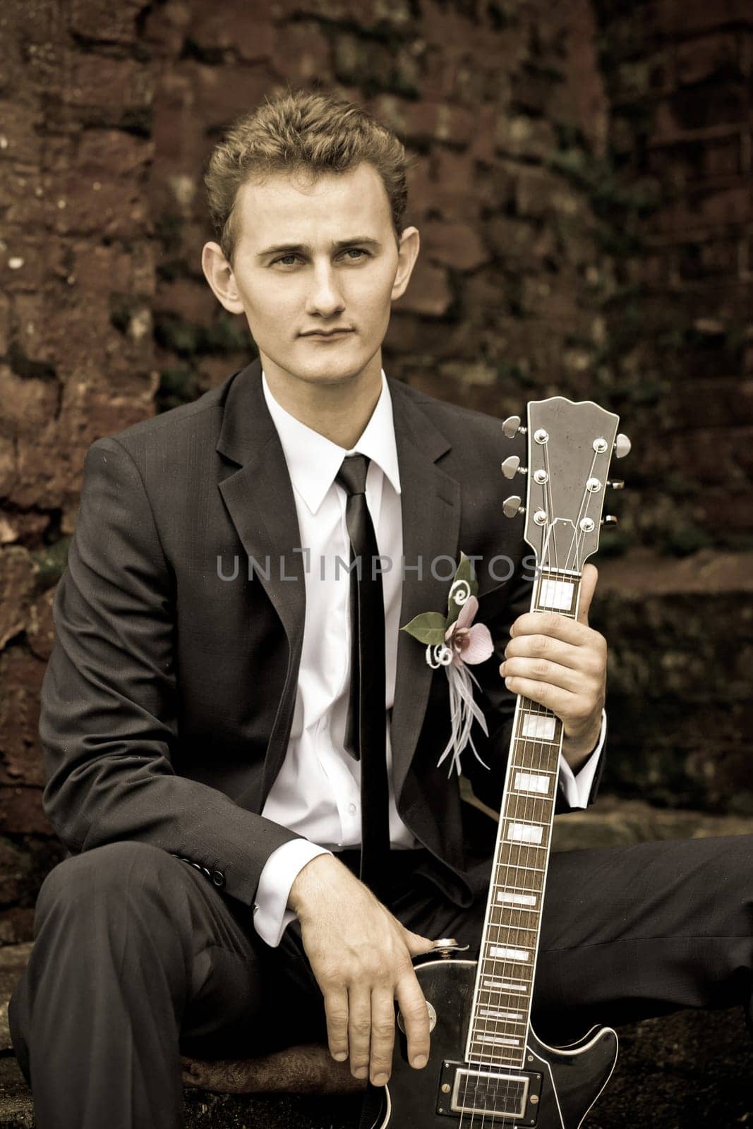A charming groom poses with his stylish guitar, showcasing charisma against a vintage backdrop enhancing the moment