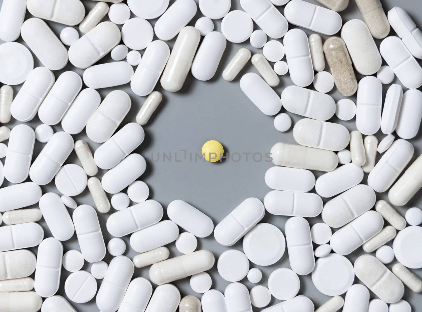 Mix of white medical capsules and pills with one yellow pill in the middle on grey top view. Medicinal treatment. Taking dietary supplements. Assorted pharmaceutical products