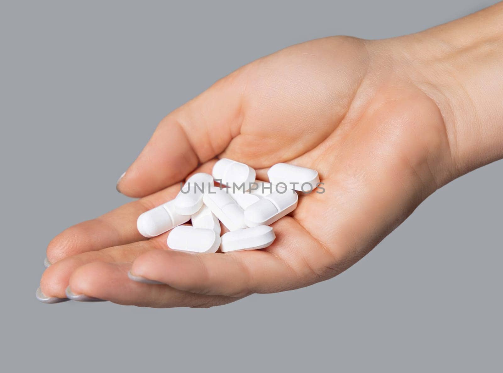 Cupped womans hand with a pile of white oval medical pills closeup over grey background. Scientific research for new pharmaceutical products.
