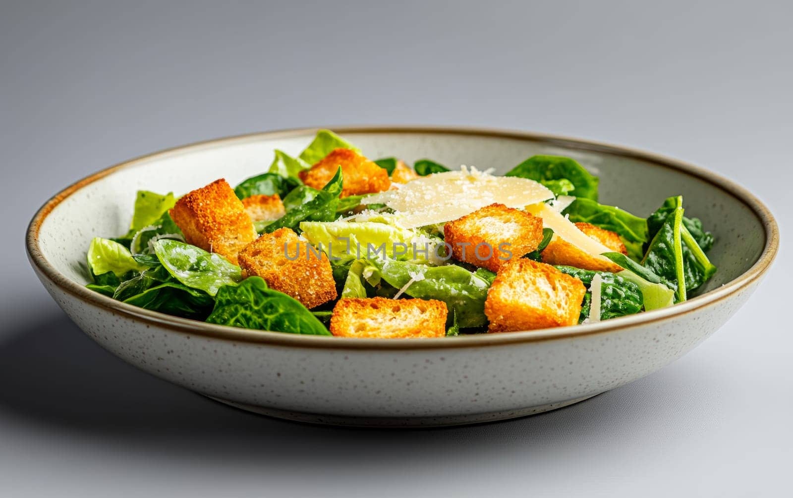 A classic Caesar salad topped with crunchy croutons and shaved Parmesan cheese, served in a rustic bowl.