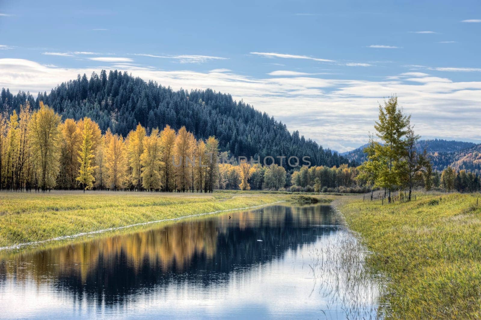 Calm water of the canal reflects the clouds in the partly blue sky on an autumn day near Bonners Ferry, Idaho.