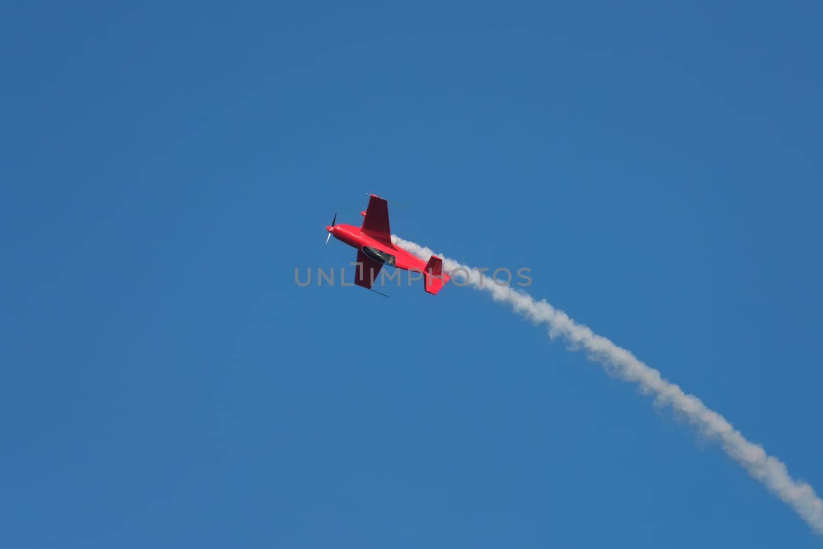 Red stunt aerobatic plane in inverted flight performing stunts in blue sky. Concept of speed, difficulty, precision, risk