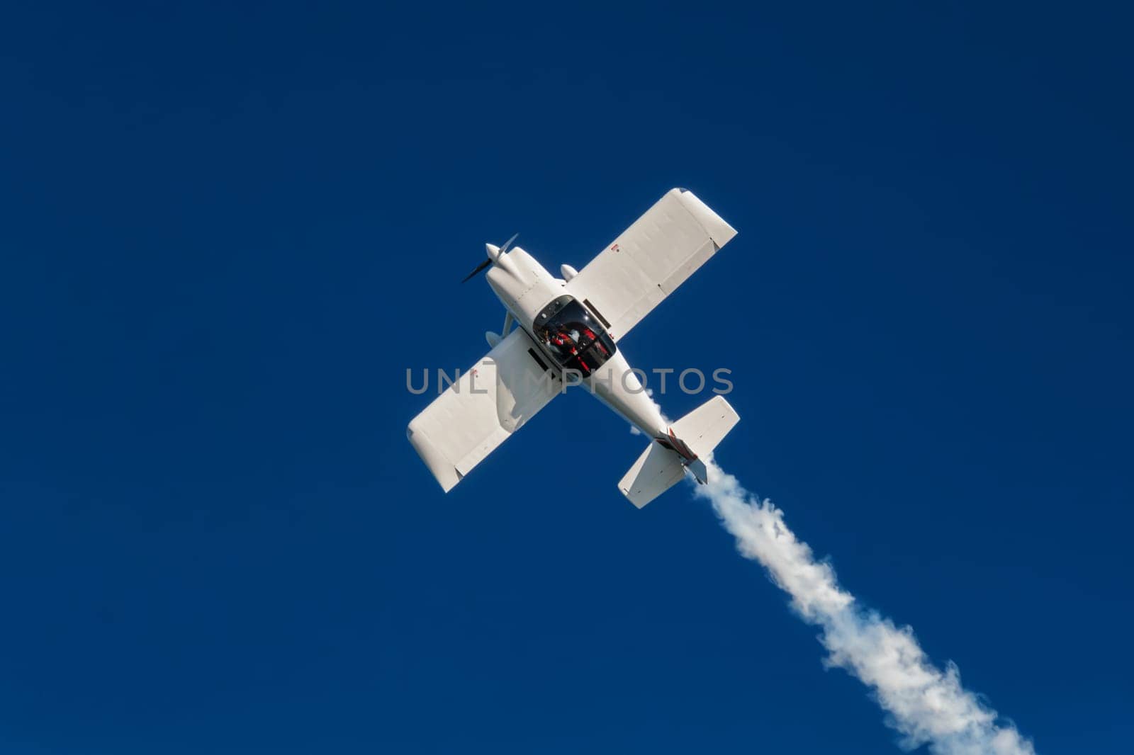 Stunt aerobatic plane inverted flying performing stunts in blue sky. Concept of speed, difficulty, precision, risk, challenge