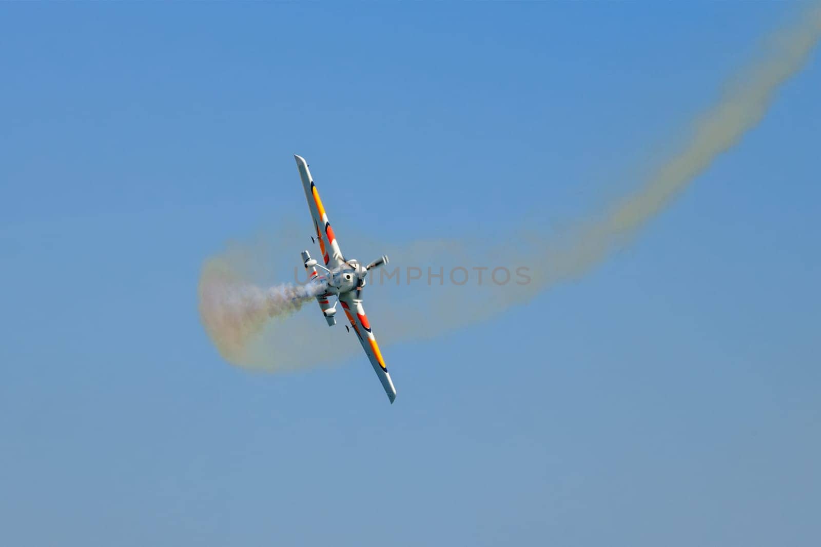 Stunt aerobatic plane performing stunts in blue sky with smoke trail. Concept of speed, difficulty, precision, risk, challenge