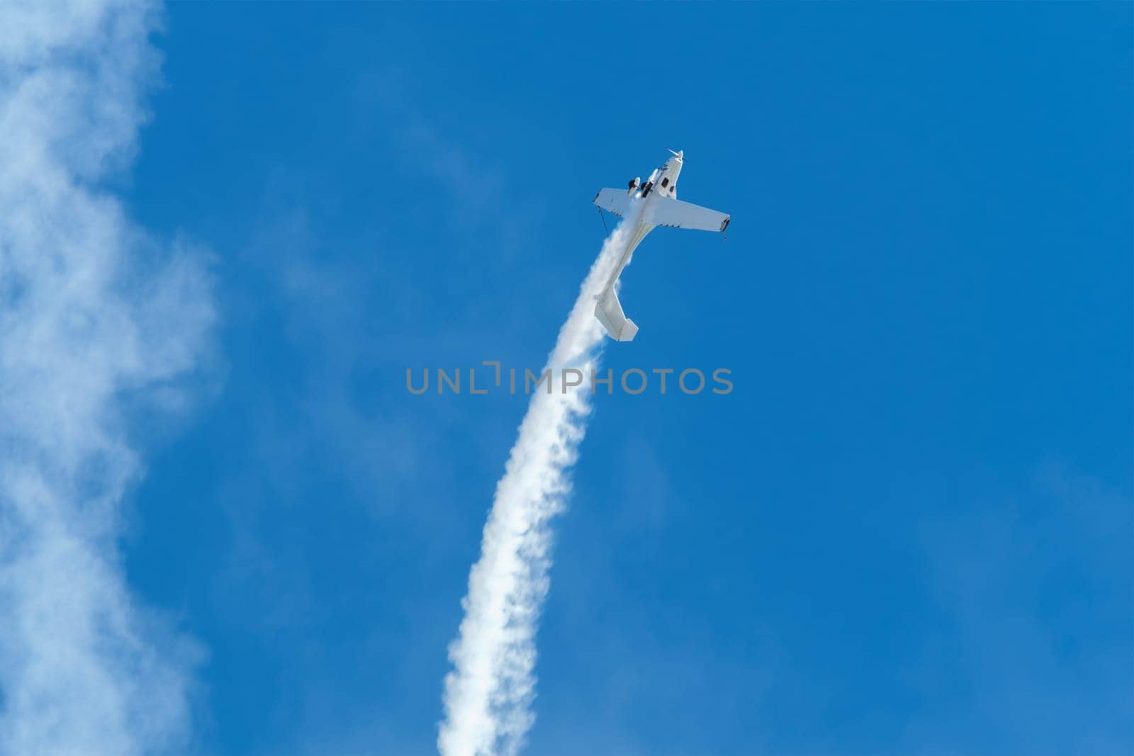 Stunt aerobatic plane performing loop in blue sky with smoke trail. Concept of speed, difficulty, precision, risk, challenge