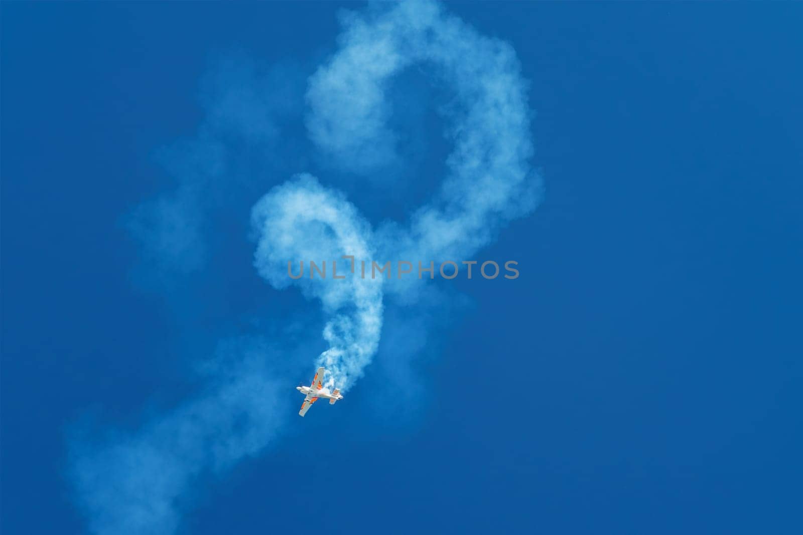 Stunt aerobatic plane performing stunts rolls loops in blue sky with smoke trail. Concept of speed, difficulty, precision, risk, challenge