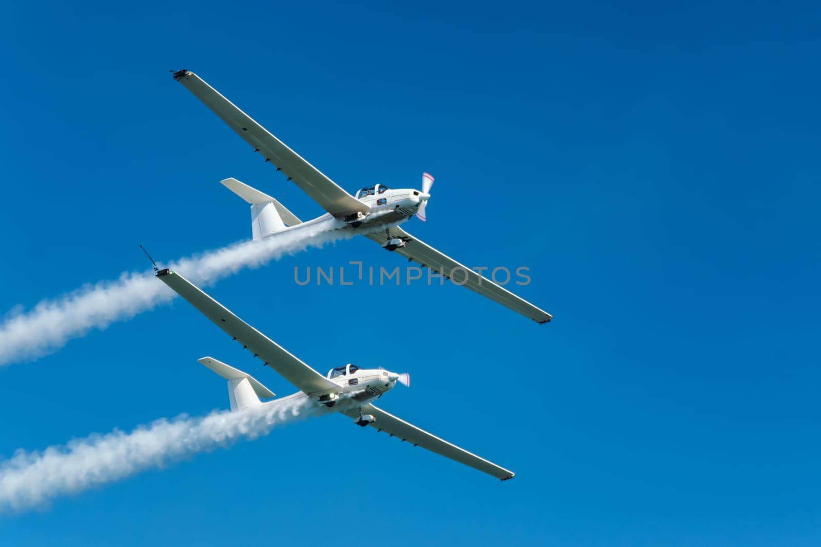 Stunt aerobatic plane performing stunts in blue sky with smoke trail. Concept of teamwork, collaboration, coordination, trust, precision, difficulty, challenge, speed, synergy