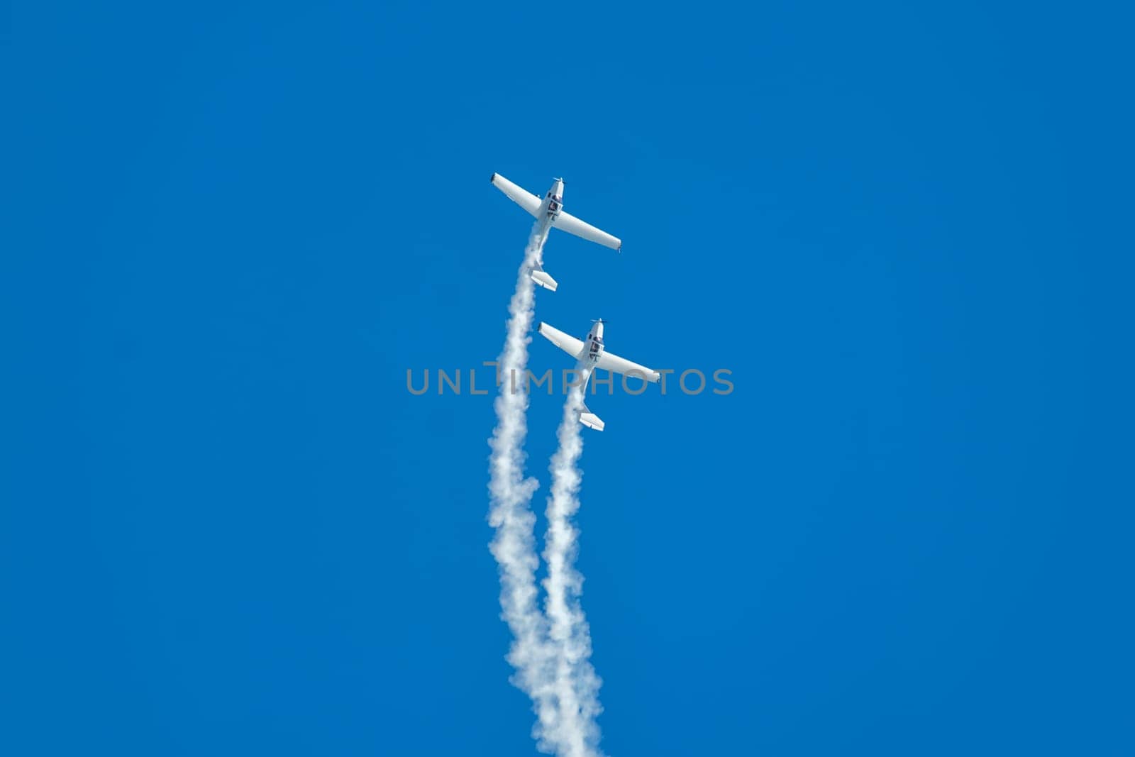 Stunt aerobatic plane performing stunts in blue sky with smoke trail. Concept of teamwork, collaboration, coordination, trust, precision, difficulty, challenge, speed, synergy