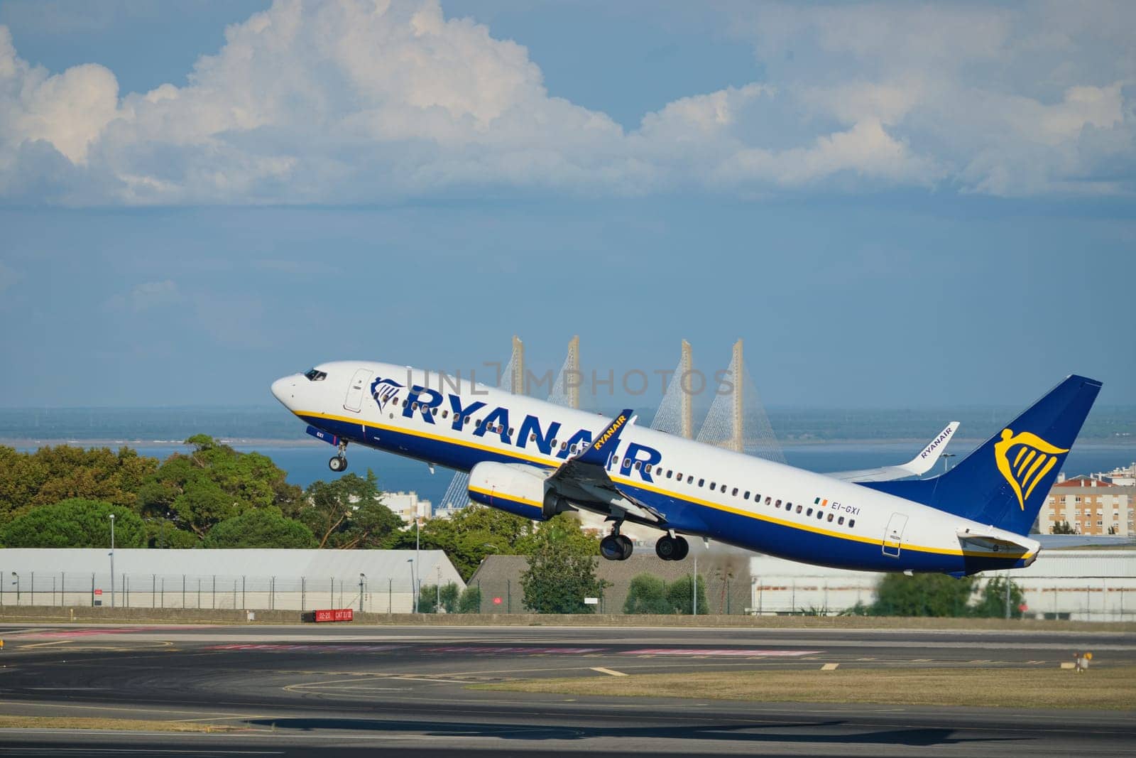 Lisbon, Portugal - September 2, 2023: Ryanair Boeing 737-8AS passenger plane take off in Humberto Delgado Airport in Lisbon with Vasco da Gamma bridge in background