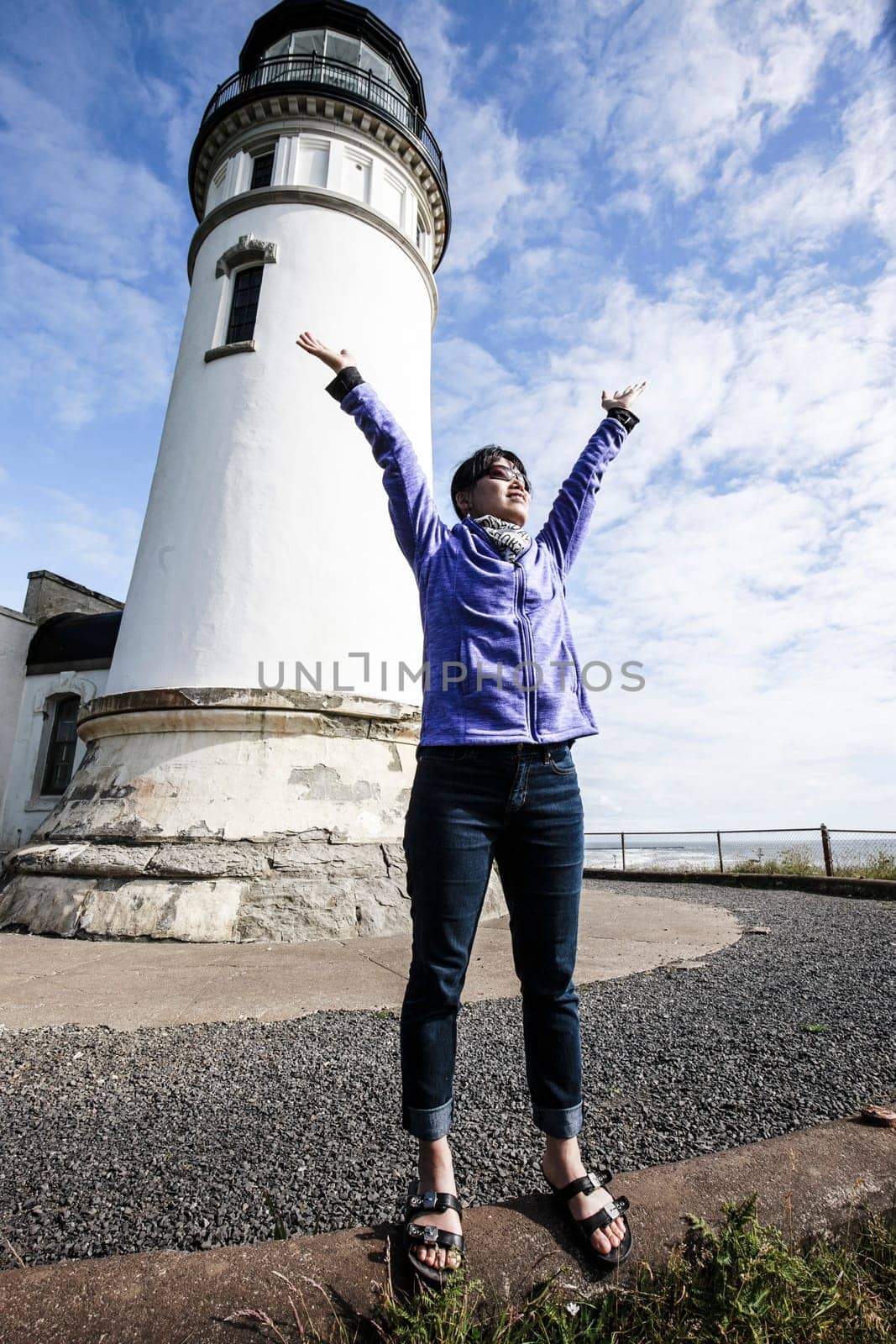 Woman raises her hands in a joyful moment next to North head lighthouse in Ilwaco, Washington.